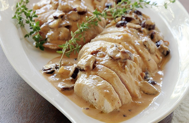 A platter of sliced turkey with cranberries, chipotle sauce and rosemary garnish.